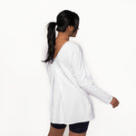 Woman wearing white long sleeve shirt with a long length relaxed fit, front scoop neckline or v-neckline with pleating and side slits paired with tight black bike shorts