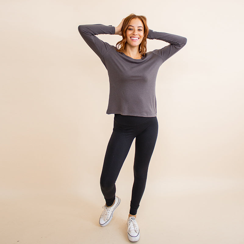 Woman wearing tight fitted black stretchy leggings with horizontal ribbing on knees featuring zippers on the back pockets and ankle and grey long sleeve shirt