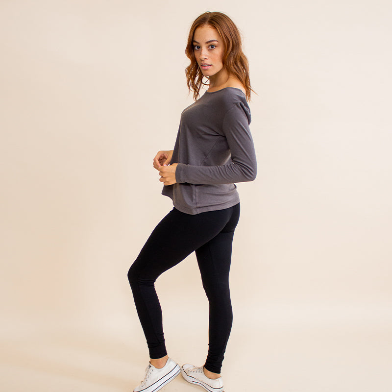 Woman wearing tight fitted black stretchy leggings with horizontal ribbing on knees featuring zippers on the back pockets and ankle and grey long sleeve shirt