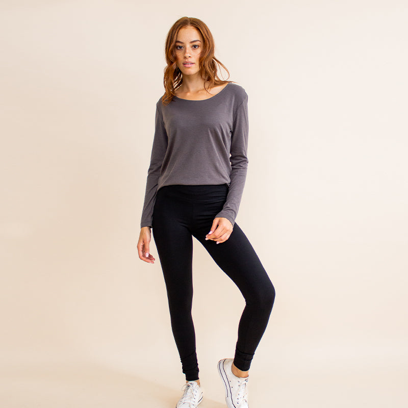 Woman wearing tight fitted black stretchy leggings with horizontal ribbing on knees featuring zippers on the back pockets and ankle and grey long sleeve shirt