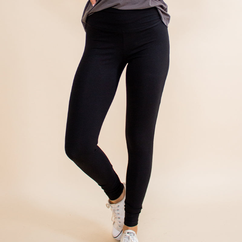 Woman wearing tight fitted black stretchy leggings with horizontal ribbing on knees featuring zippers on the back pockets and ankle