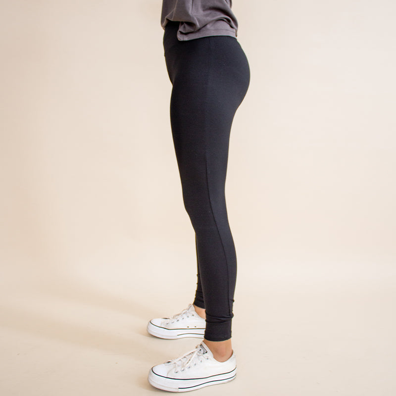 Woman wearing tight fitted black stretchy leggings with horizontal ribbing on knees featuring zippers on the back pockets and ankle