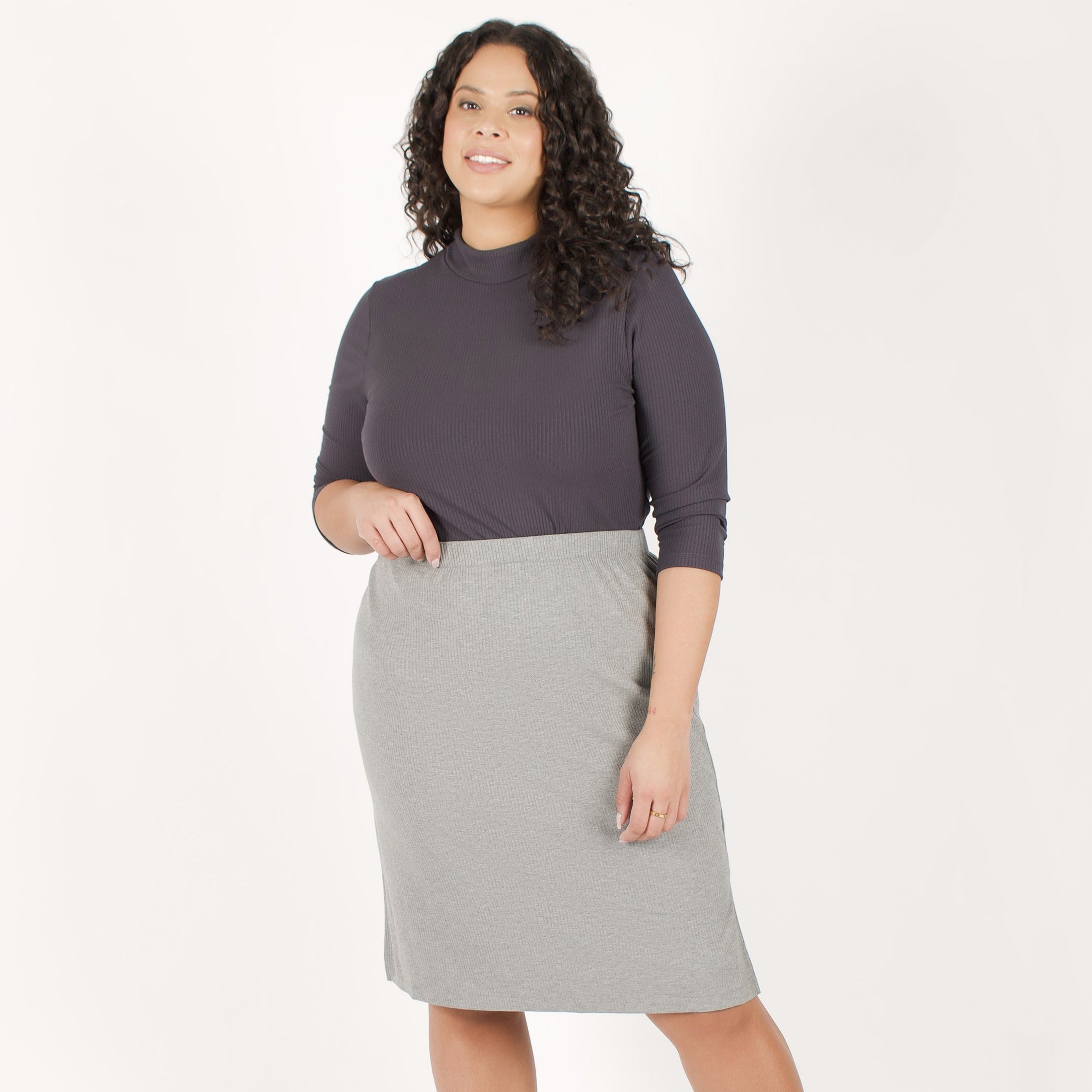 Woman wearing grey body-skimming fit stretchy mid calf length vertical ribbed skirt paired with dark grey mock neckline long sleeve ribbed shirt
