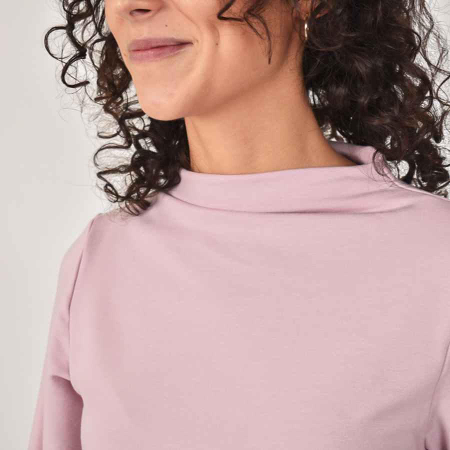 Woman wearing light pink loose blouse with puffy long sleeve and funnel neckline