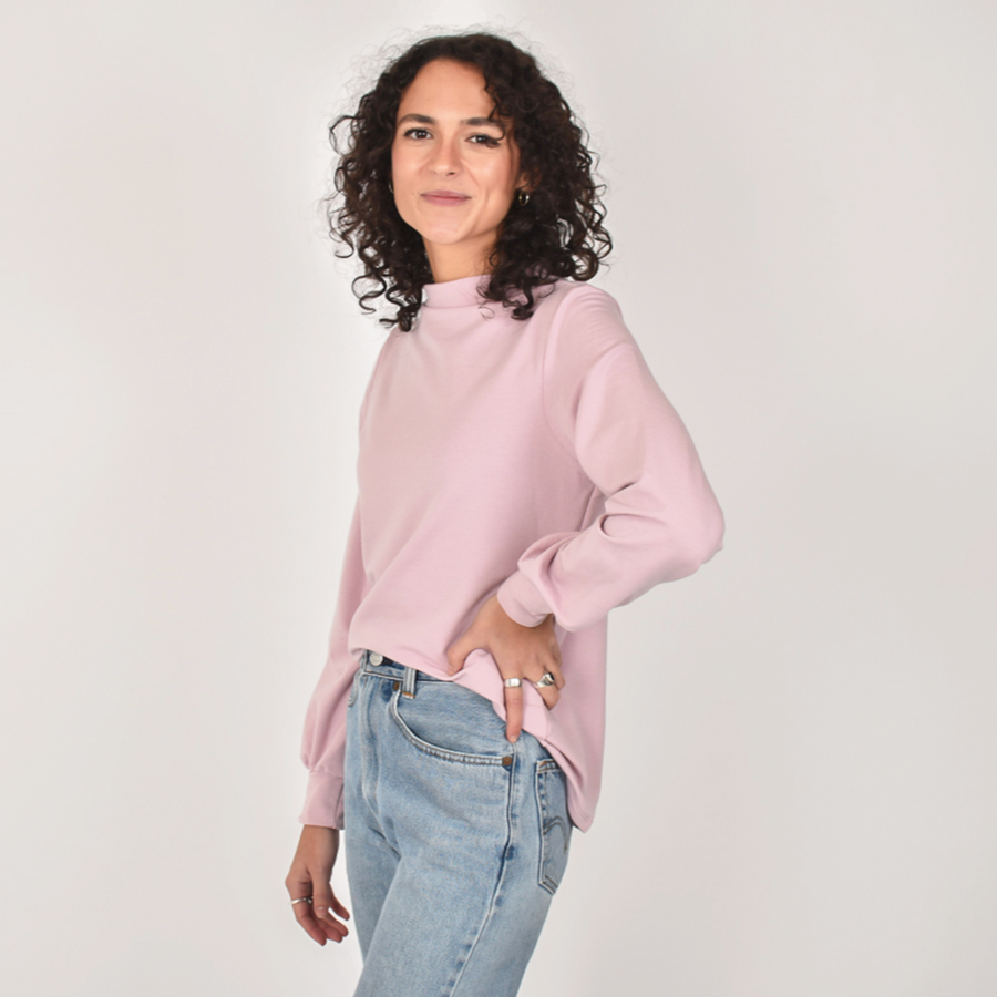 Woman wearing light pink loose blouse with puffy long sleeve and funnel neckline with light blue jeans