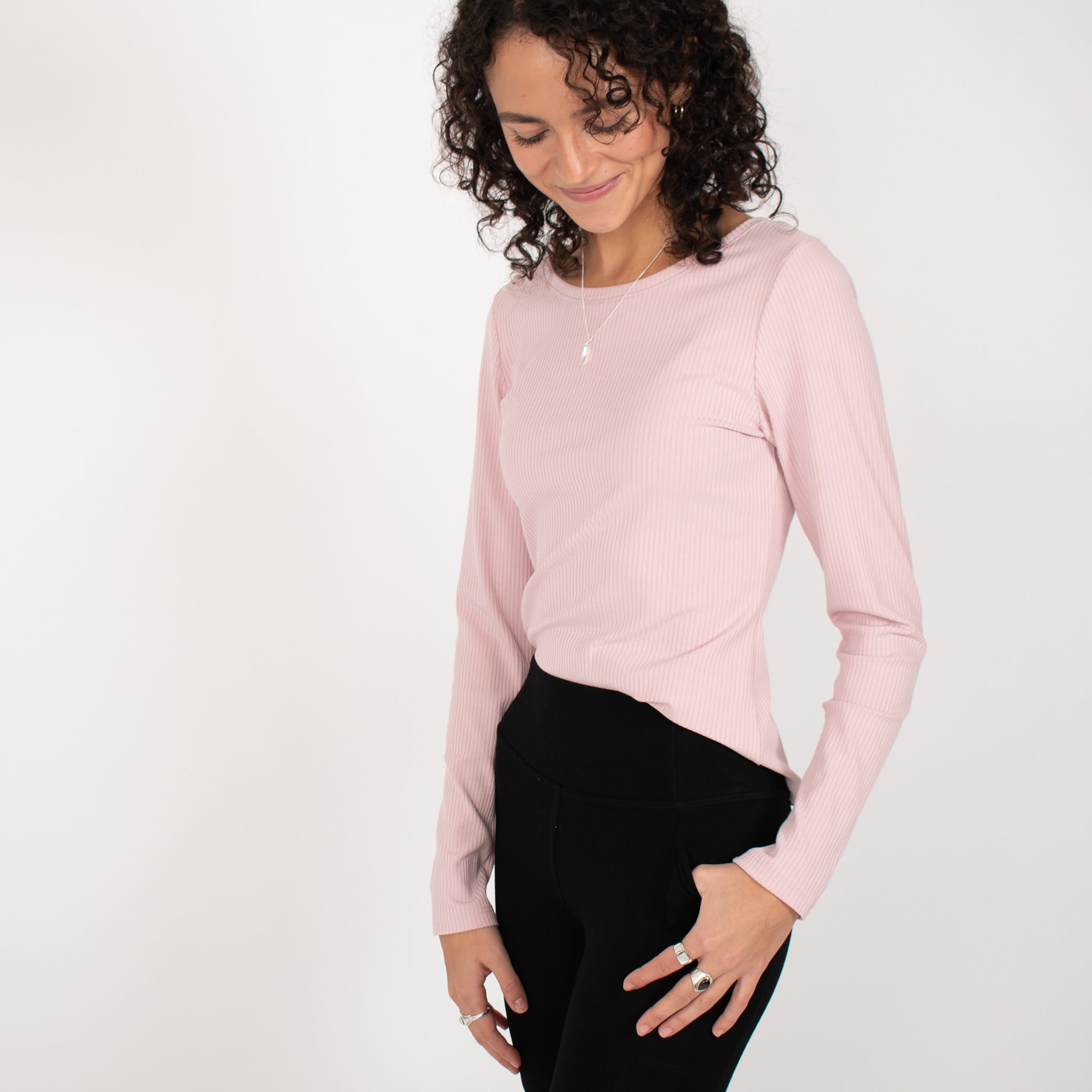 Woman wearing light pink rib knit reversible long sleeve top with black tapered leggings