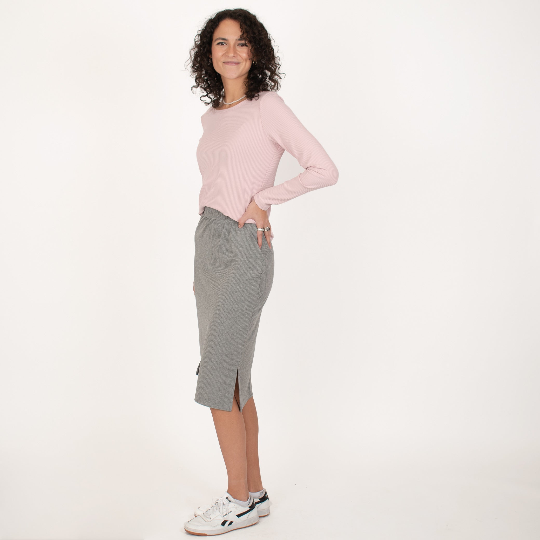 Woman wearing light pink rib knit reversible long sleeve top with grey knee length skirt
