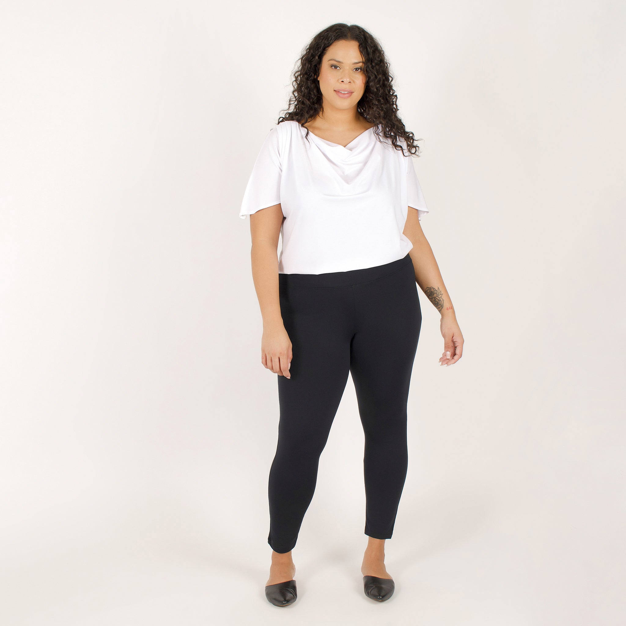 Woman wearing fitted black high-rise waist with ankle length leggings featuring seamless stitching and a hidden back pocket with loose white shirt