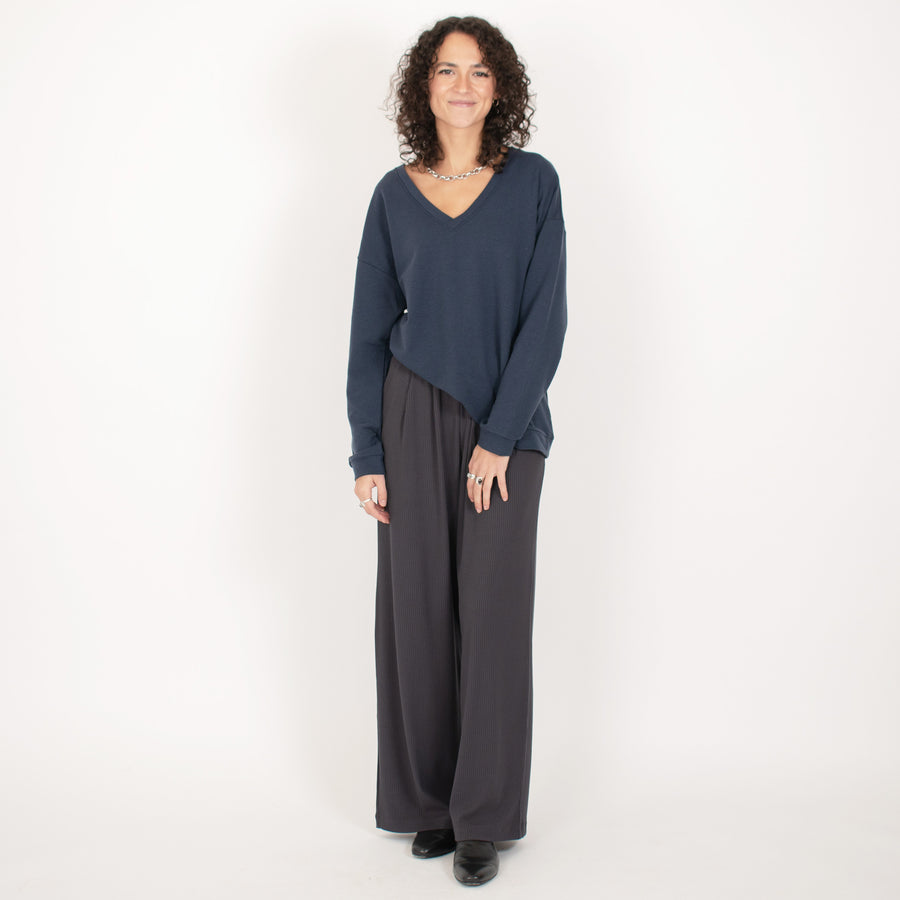 Woman wearing reversible navy blue v-neckline loose sweatshirt with dark grey wide leg pants