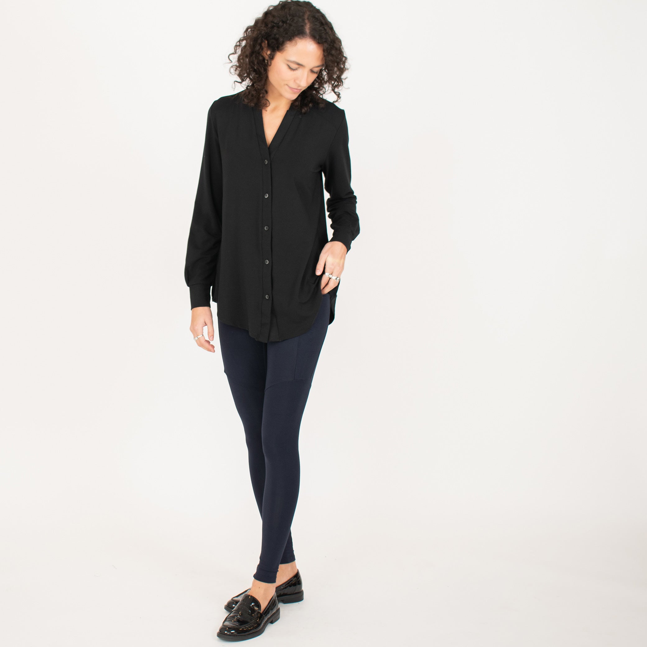 Woman wearing navy blue form fitting stretchy leggings with hip pocket with black button up shirt