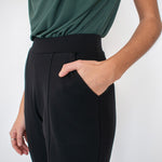 Woman wearing black tailored stretchy ankle length pants paired with tucked in green shirt