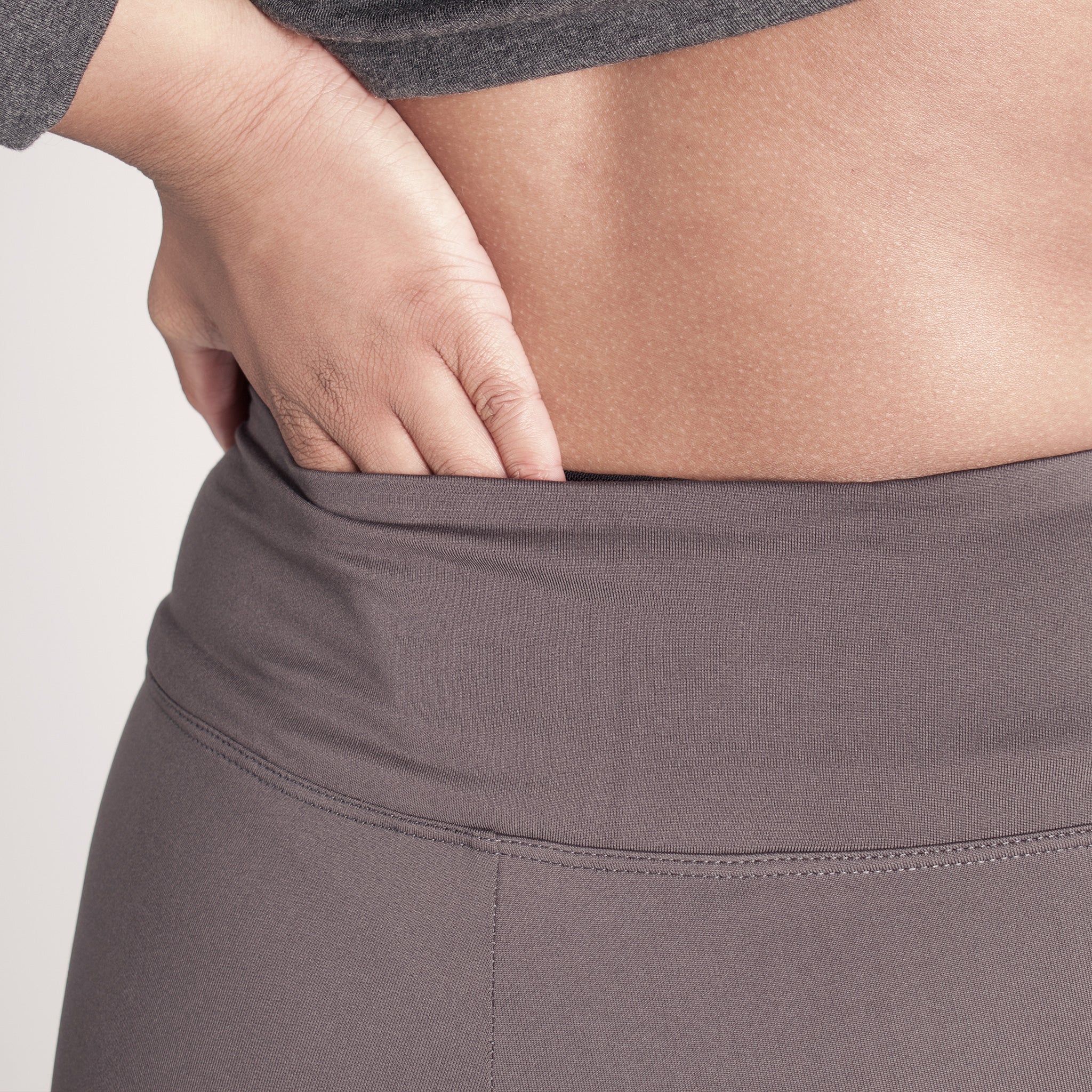 Woman wearing fitted light brown high-rise waist with ankle length leggings featuring seamless stitching and a hidden back pocket 