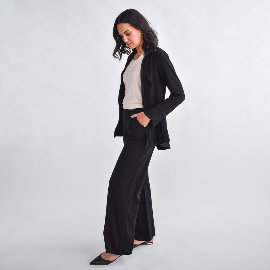 Woman wearing fitted navy stretchy front zippered jacket open with cream shirt and black wide leg pants with pockets